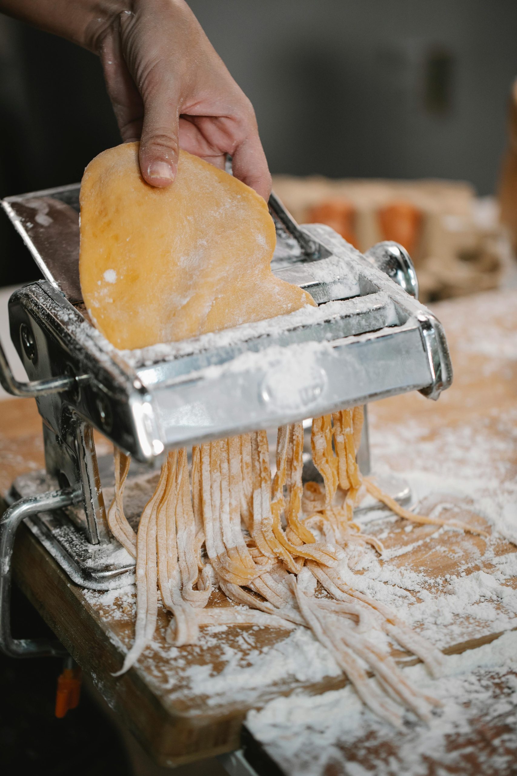Una macchina per la pasta manuale crea tagliatelle di pasta fresca ripiena su un tagliere infarinato
